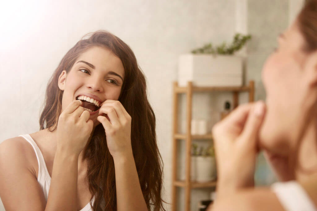 Beautiful woman is using dental floss in the morning