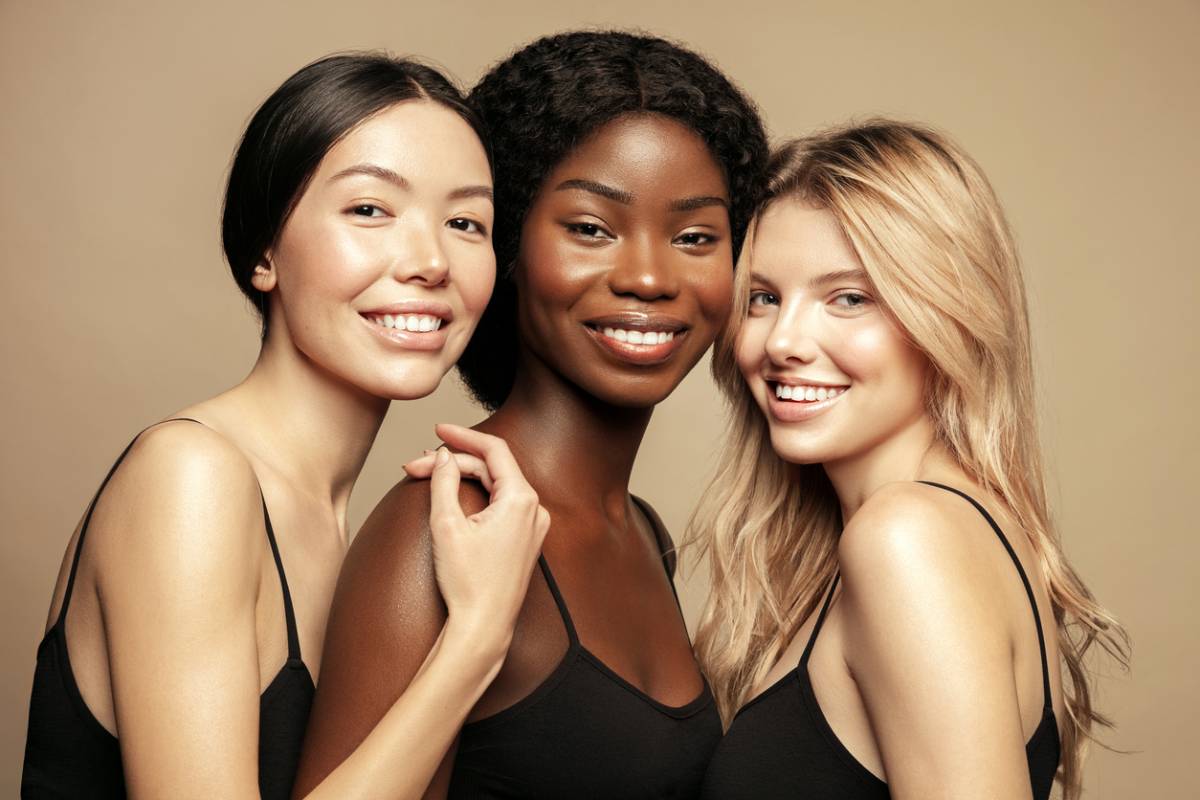 3 woman in black dresses smiling, one asian, one black, and one white